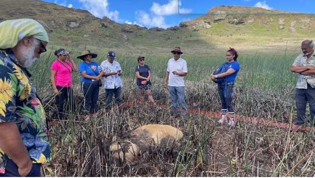 Pesquisadores analisando estátua Moai encontrada no fundo de um lago seco.